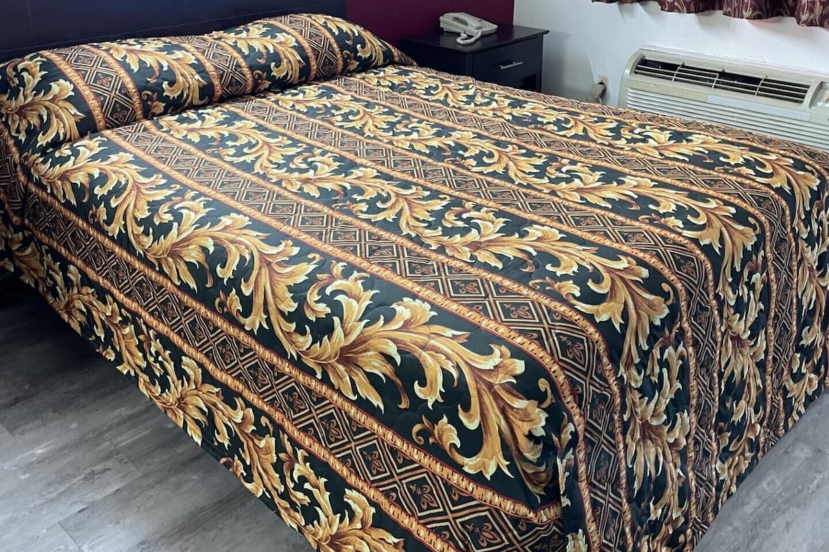 Ett hotellrum med ett mönstrat överkast på sängen, en telefon vid sängen och en väggmonterad luftkonditioneringsanläggning.