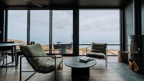 Ein modernes Interieur mit großen Fenstern, einem runden Couchtisch, zwei Sesseln und einem Kamin.