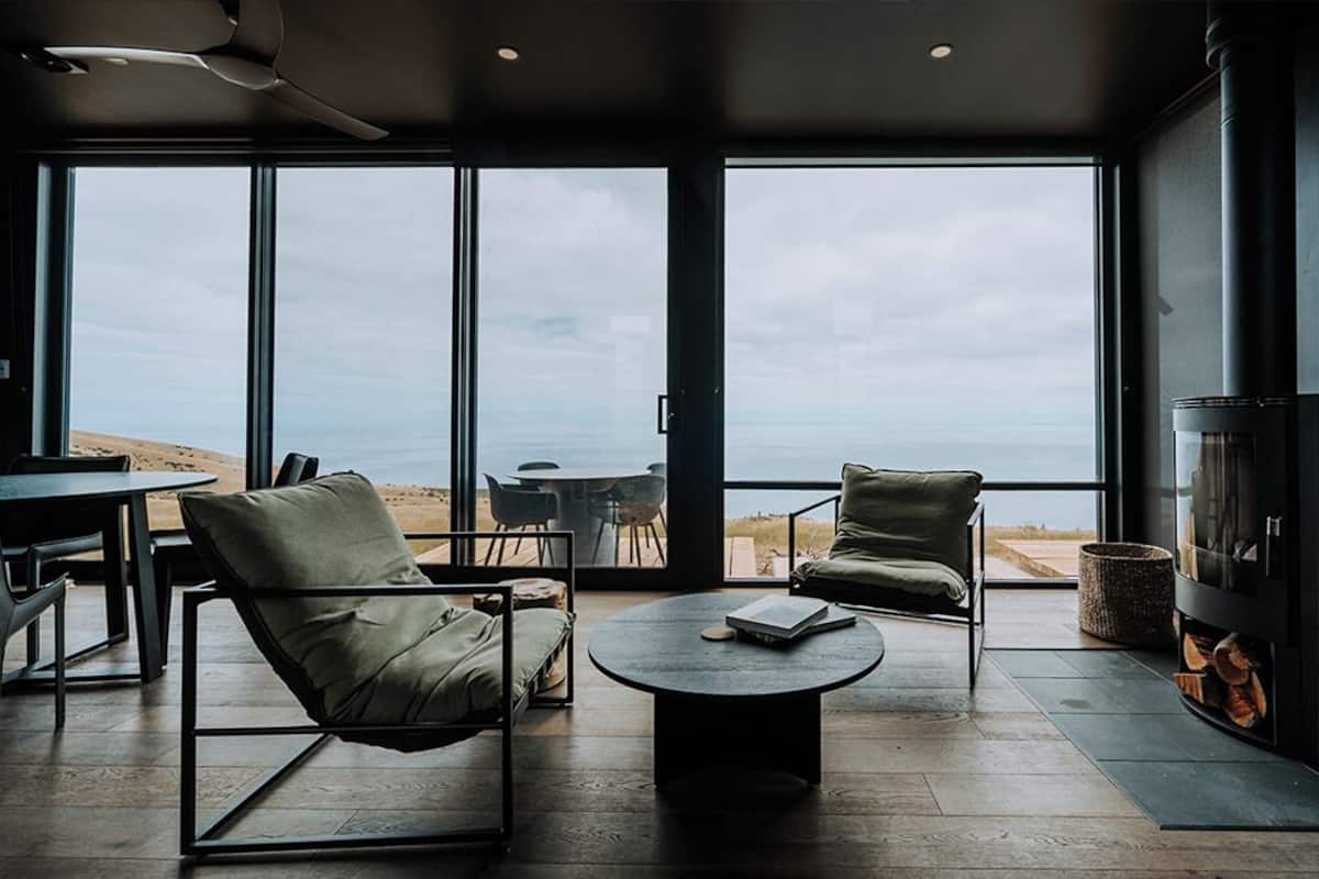 A modern interior with large windows, a round coffee table, two armchairs, and a fireplace.