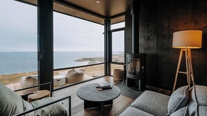 Ein modernes Wohnzimmer mit großem Fenster mit Meerblick, einem Kamin und einer gemütlichen Sitzecke.
