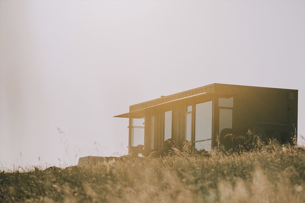 A modern, minimalist house with large windows, situated on a grassy hill.