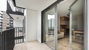 A modern apartment with a balcony, a sliding glass door leading to a kitchen, and a view of neighboring buildings. - Ursus Cosy Apartment #51 (Warszawa)