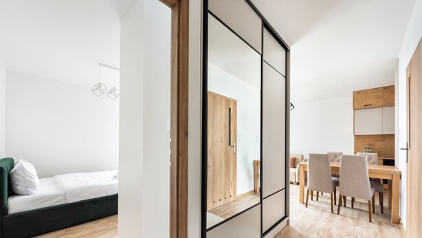 A modern, well-lit room with a bed, a dining area with a wooden table and chairs, and a large mirror reflecting the room. - Ursus Cosy Apartment #51 (Warszawa)