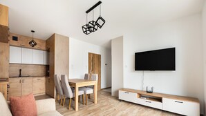 A modern living room with a wooden dining table, a sofa, and a flat-screen TV mounted on the wall. - Ursus Cosy Apartment #51 (Warszawa)