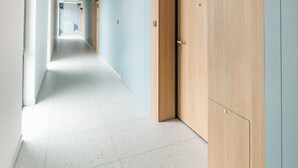 A modern hallway with a light blue wall, a wooden door labeled '70', and a white tiled floor. - Ursus Cosy Apartment #51 (Warszawa)