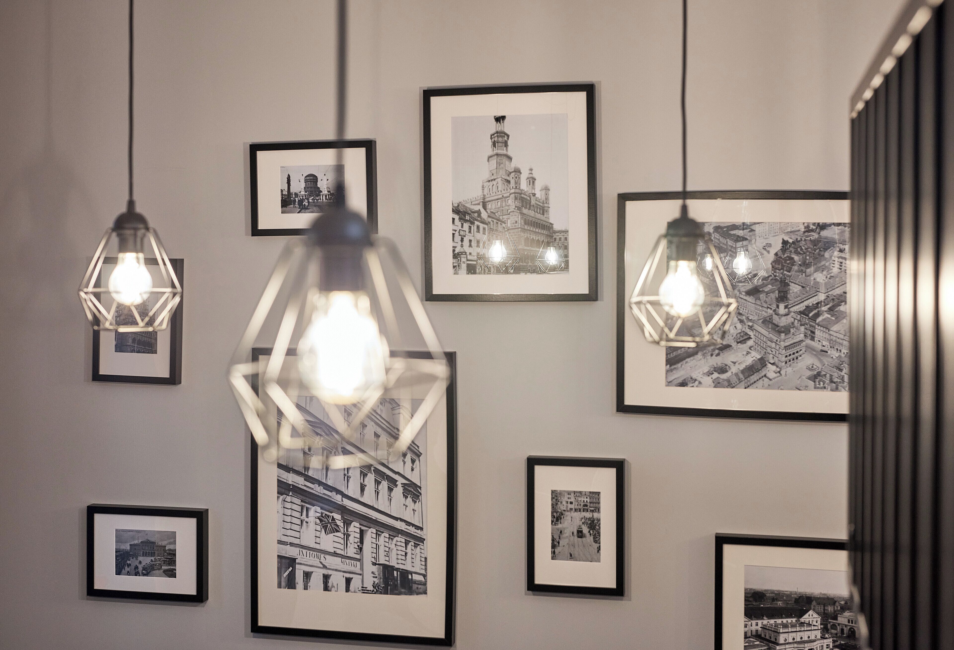 A wall with framed black and white photographs of buildings and a geometric light fixture.