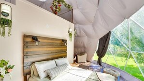 Eine Zelthütte mit Bett, Kopfteil und Blick auf die grüne Umgebung.