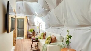 Eine Zelteinrichtung mit einer Couch, einem kleinen Tisch und einem an der Wand befestigten Fernseher.