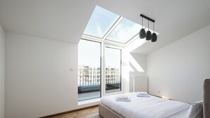 A modern bedroom with a skylight, a bed, and a view of buildings outside.