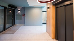 A modern hallway with a glass door, a wooden wall, and a ceiling with circular light fixtures.