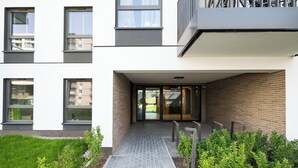 A modern building entrance with a paved walkway, glass doors, and a brick wall.