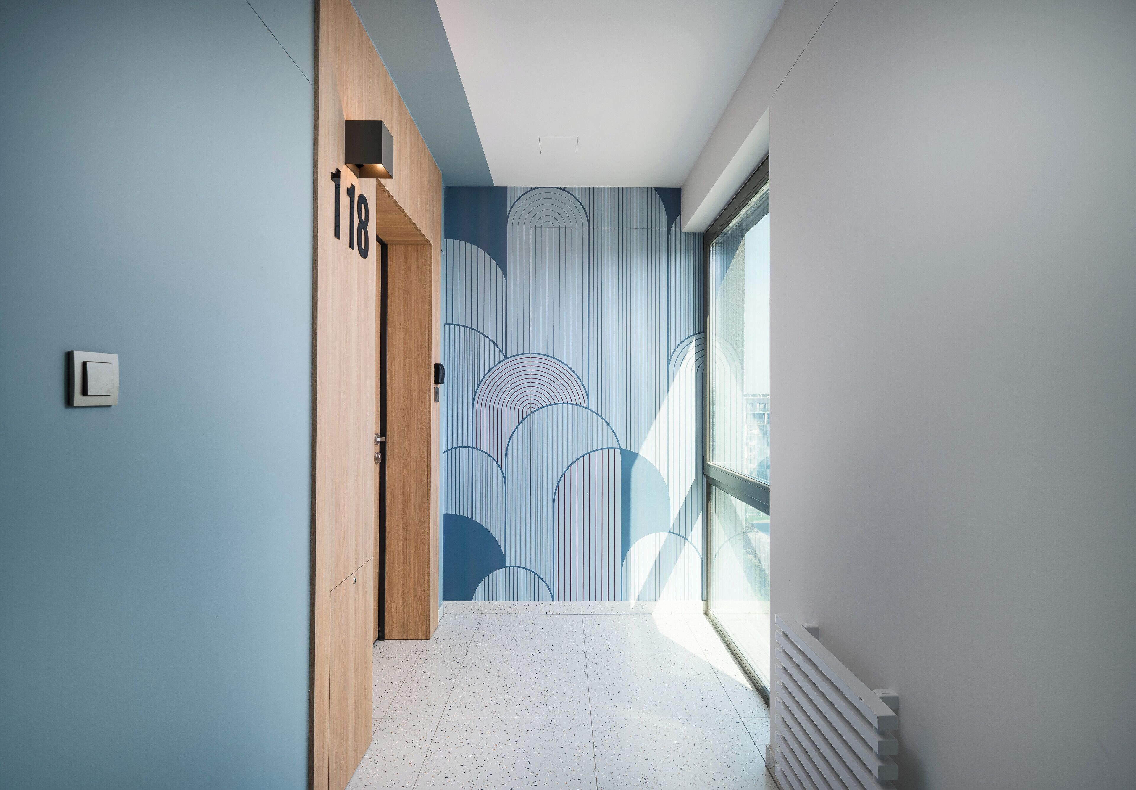 A hallway with a blue wall, a wooden door labeled "118", and a window on the right.