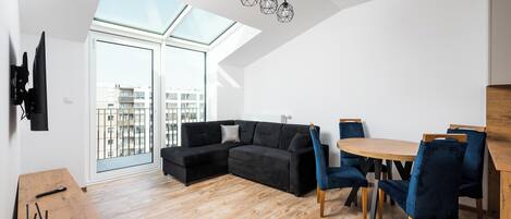 Una sala de estar moderna con un sofá seccional negro, una mesa de comedor de madera con sillas azules y un tragaluz arriba.