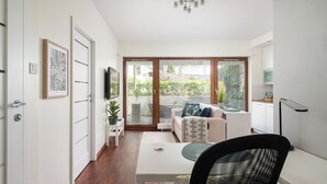 A modern living room with a white sofa, a dining table, and a black chair. There is a TV mounted on the wall and a plant on a side table. - Las Kabacki Comfy Apartment (Warszawa)