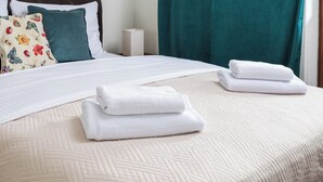 A neatly made bed with white linens and folded towels, a floral pillow, and a teal curtain. - Las Kabacki Comfy Apartment (Warszawa)
