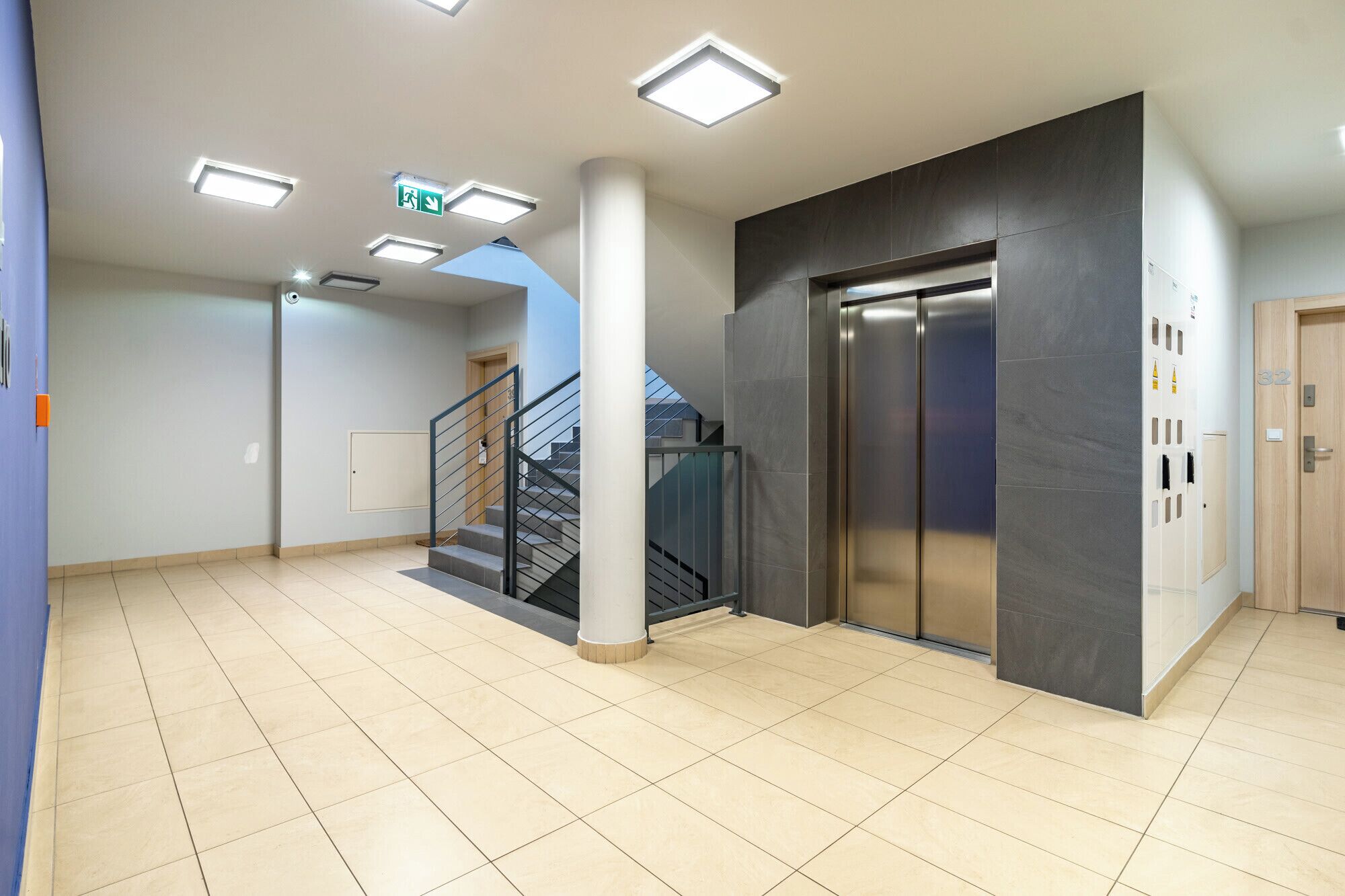 Un interior moderno con una escalera, un ascensor y piso de baldosas.