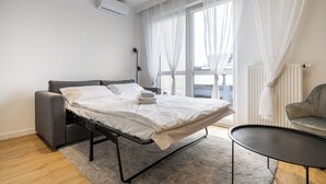Une chambre d’hôtel moderne, équipée d’un lit, d’une petite table, d’une chaise et d’une fenêtre avec des rideaux légers.