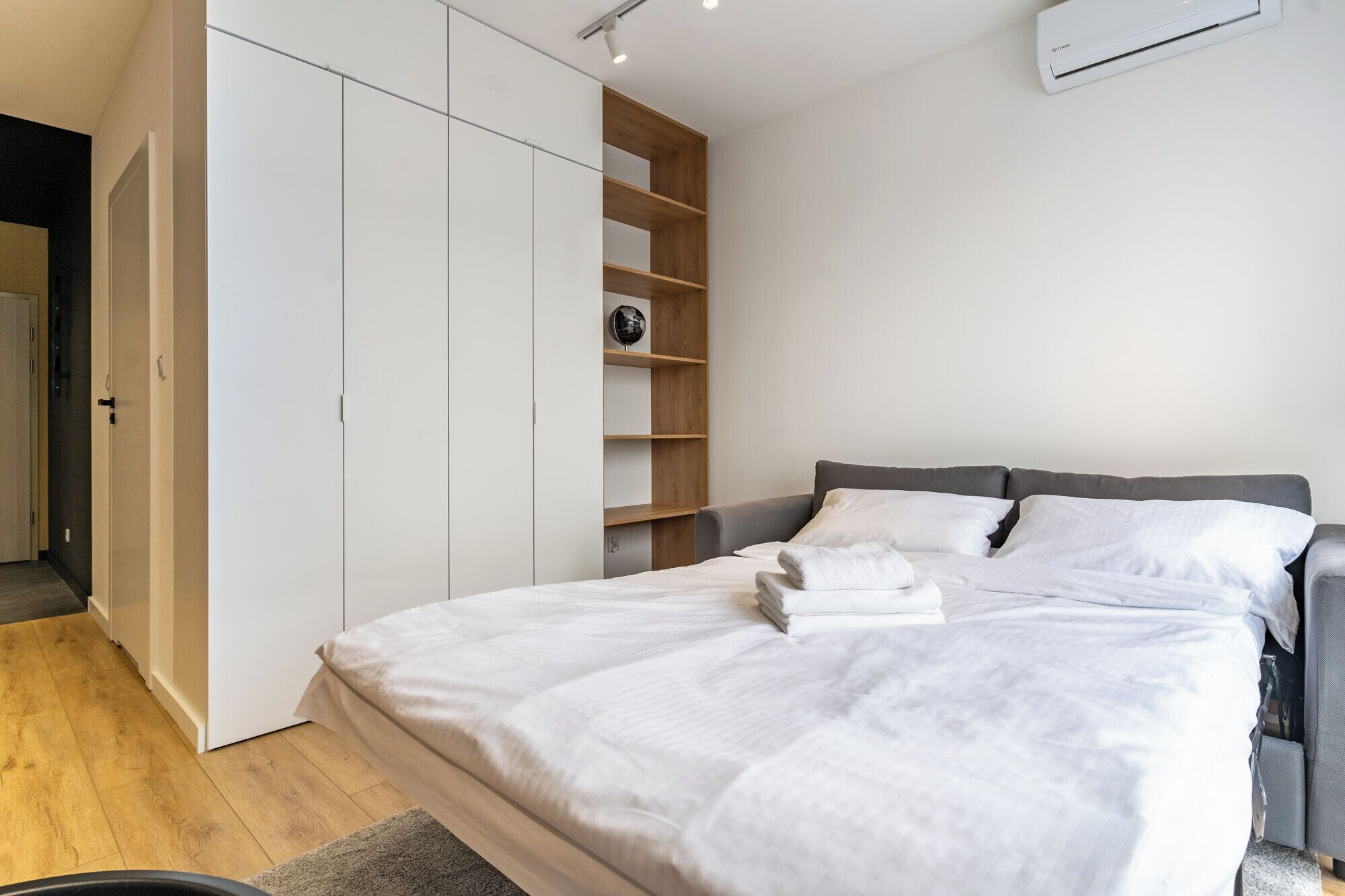 A modern bedroom with a large bed, a wardrobe, and a shelf unit.