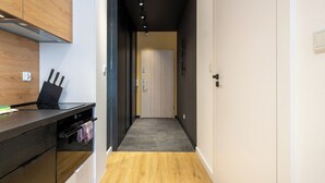 Un couloir étroit avec un plancher en bois, un coin cuisine doté d’un comptoir noir et d’un bloc à couteaux, et une porte donnant sur une autre pièce.