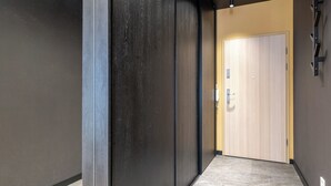 Un couloir aux murs sombres, une porte de couleur claire et un sol carrelé.