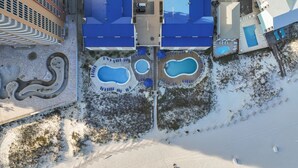 Eine Vogelperspektive auf ein Hotel mit mehreren Gebäuden mit blauen Dächern, einem zentralen Schwimmbereich mit Pools und einer verschneiten Landschaft.