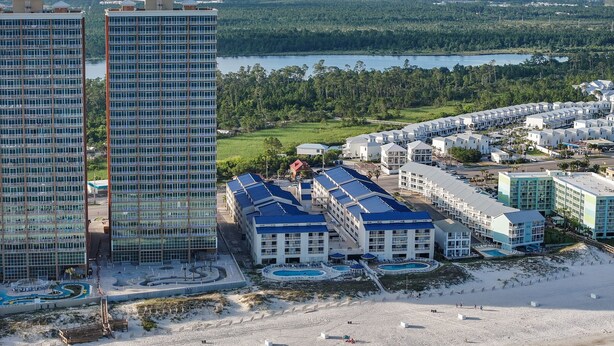 Ein Küstenhotel mit mehreren Gebäuden, einem Strand und einem See im Hintergrund.