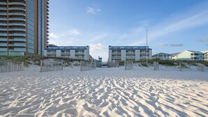 Ein Sandstrand mit einer Holzlattenzaun und einer Reihe von Gebäuden im Hintergrund.