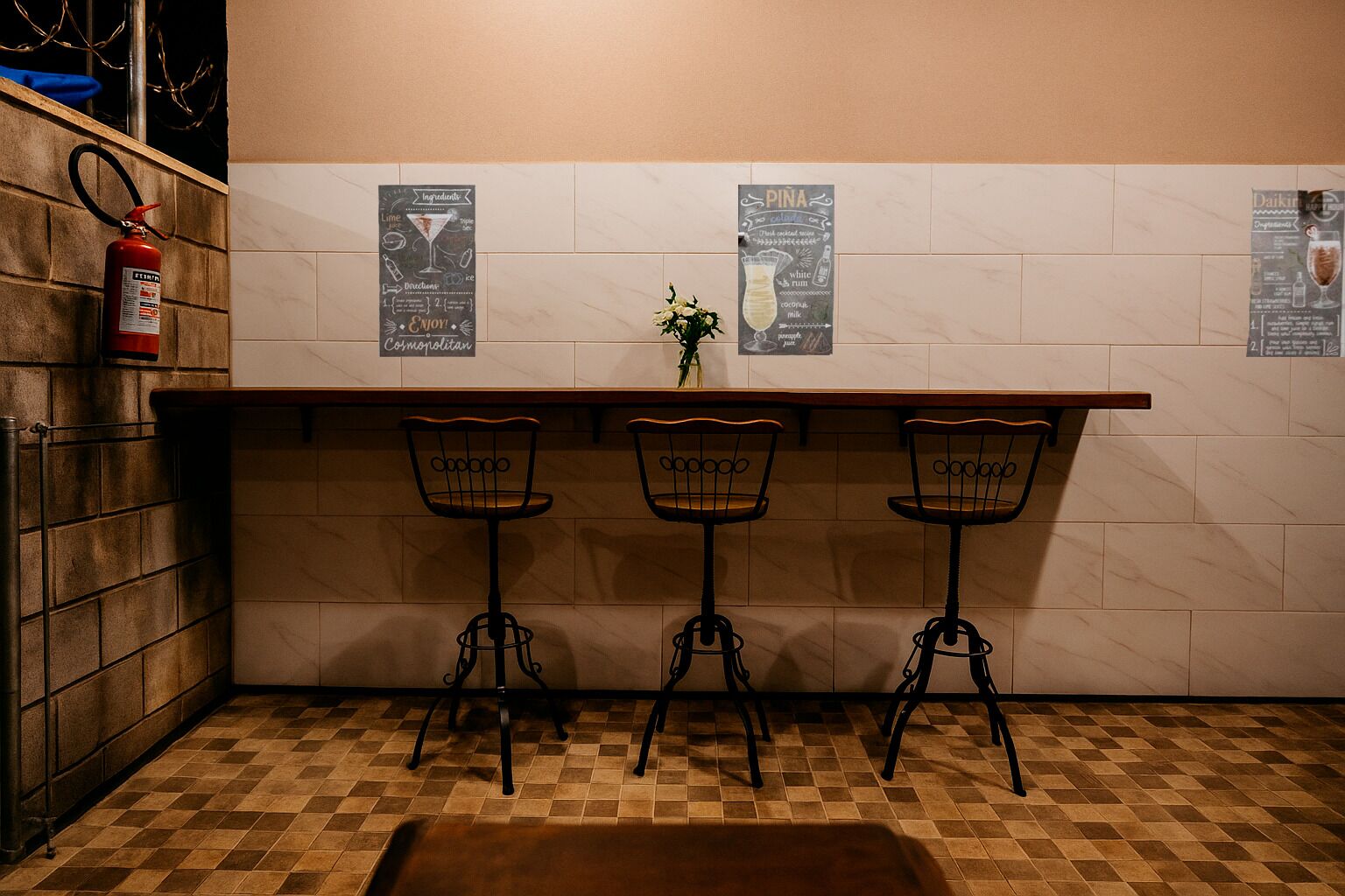 Un espace bar avec trois tabourets, un extincteur et un mur où sont affichés les menus.