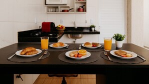 A breakfast setup with croissants, toast, tomatoes, and orange juice on a dark kitchen table. - Olímpia Aparts  (Olímpia)