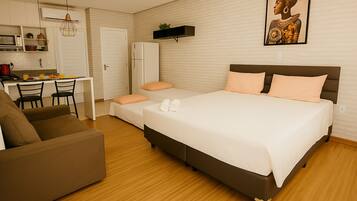 A hotel room with a bed, a sofa, a desk with a chair, a microwave, and a refrigerator.