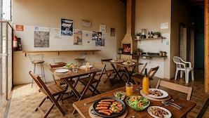 A dining area with wooden tables and chairs, a brick oven, and various food items on the tables. - Olímpia Aparts  (Olímpia)