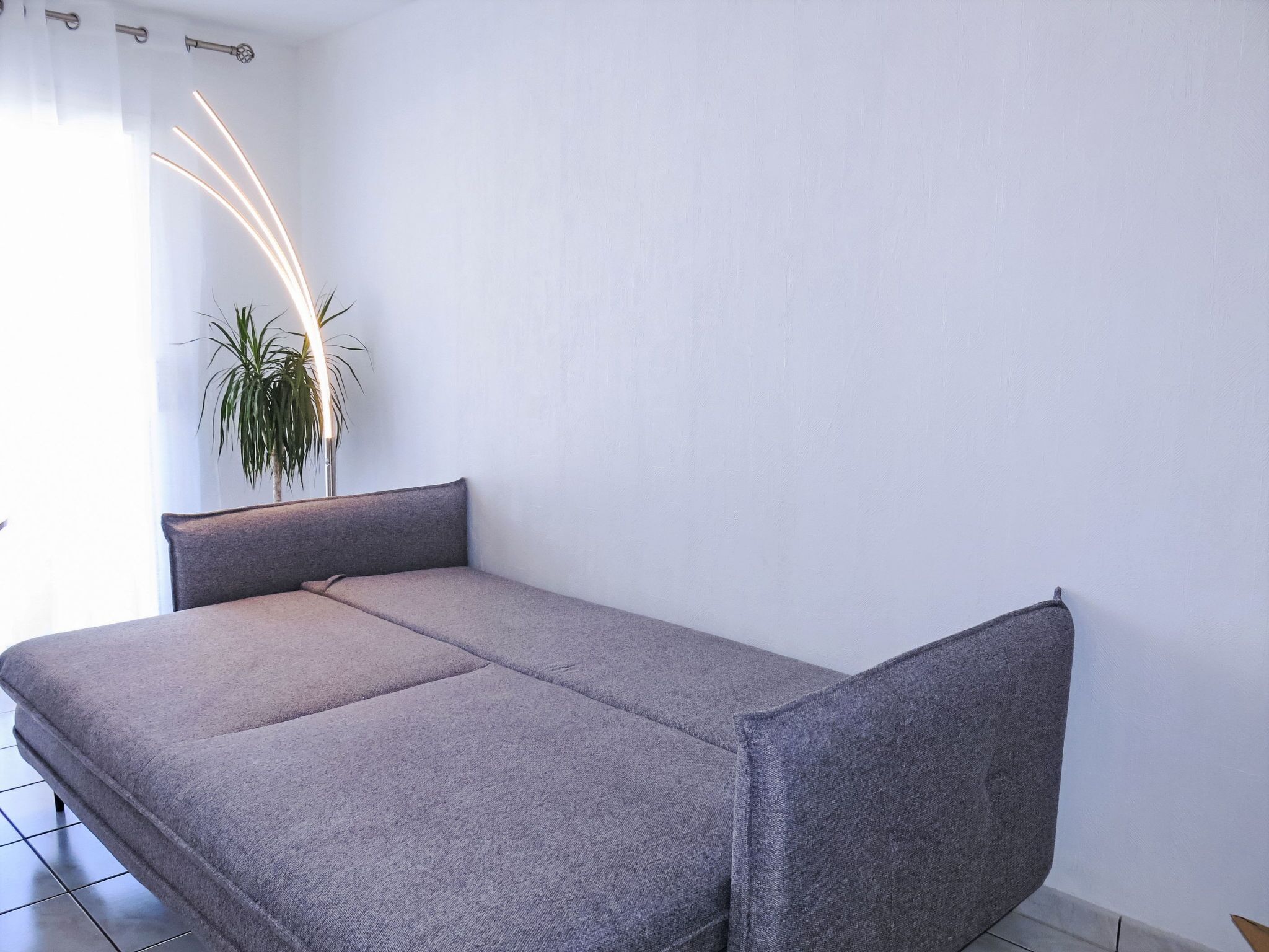 Ein kleiner, moderner Raum mit einem grauen Sofa, einem Blumentopf und einer weißen Wand.