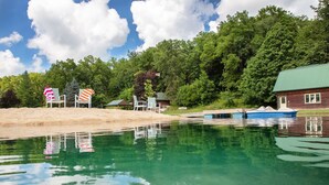 A lakeside cabin with a dock, a small boat, and a beach area with chairs. - Modern Cottage Cabin, private area with pond, fishing nearby, swimming and more  (McGregor)