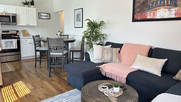 Ein modernes Wohnzimmer mit einem dunkelblauen Sofa, einem runden Holztisch und einem Essbereich mit weißem Tisch und Stühlen.