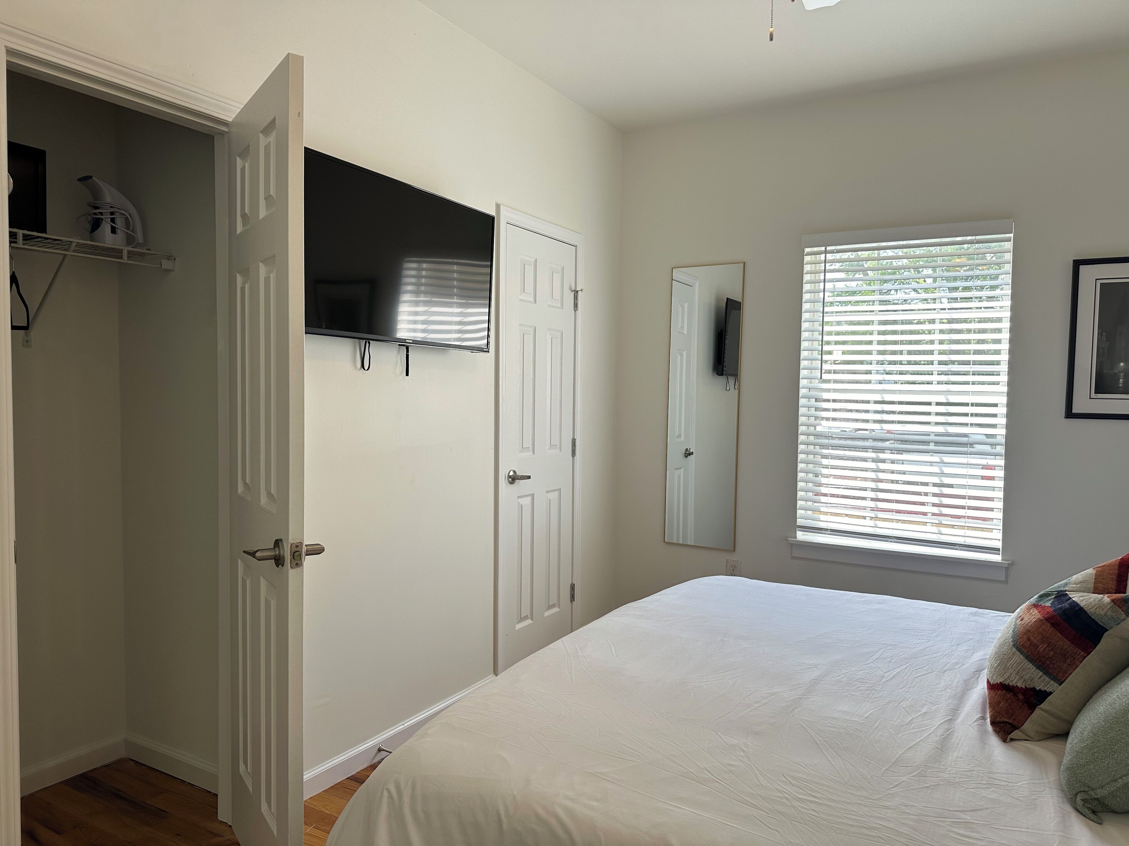 A bedroom with a bed, a wardrobe, a TV, and a window with blinds.