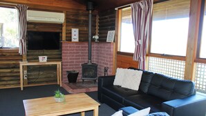 A cozy cabin interior with a fireplace, a black leather sofa, a wooden coffee table, and a television. - Cosy cabin in the Grampians with mountain views (Wartook)