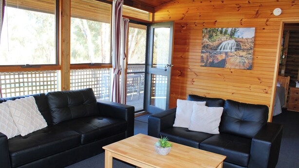 A room with two black leather sofas, a wooden coffee table, and a painting of a waterfall on the wall. - Cosy cabin in the Grampians with mountain views (Wartook)