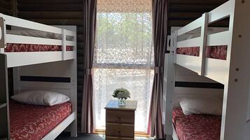 A room with two bunk beds, a small wooden dresser, and a window with lace curtains.