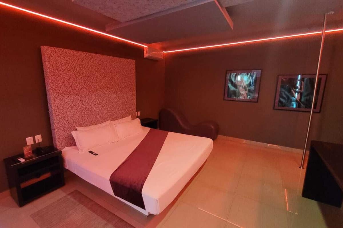 A modern bedroom with a large bed, a nightstand, a chair, and a TV.