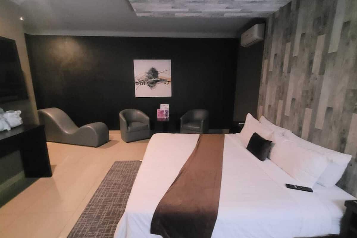 A modern hotel room with a large bed, two armchairs, a small table, and a wall-mounted artwork.