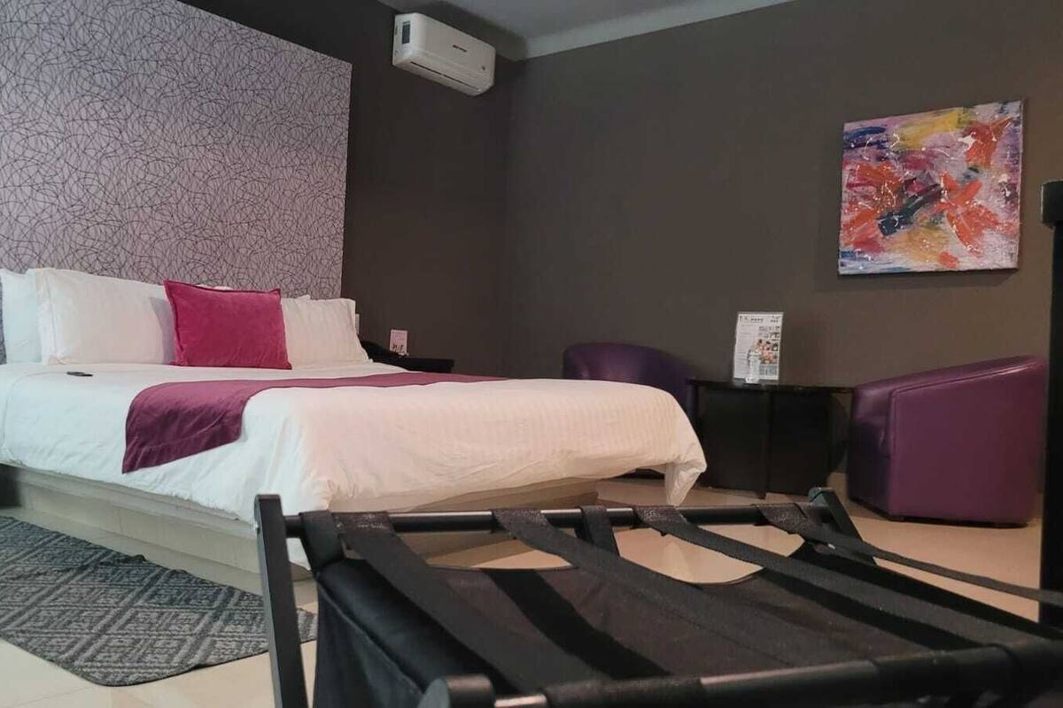 A modern hotel room with a large bed, a desk, a chair, and a purple ottoman.