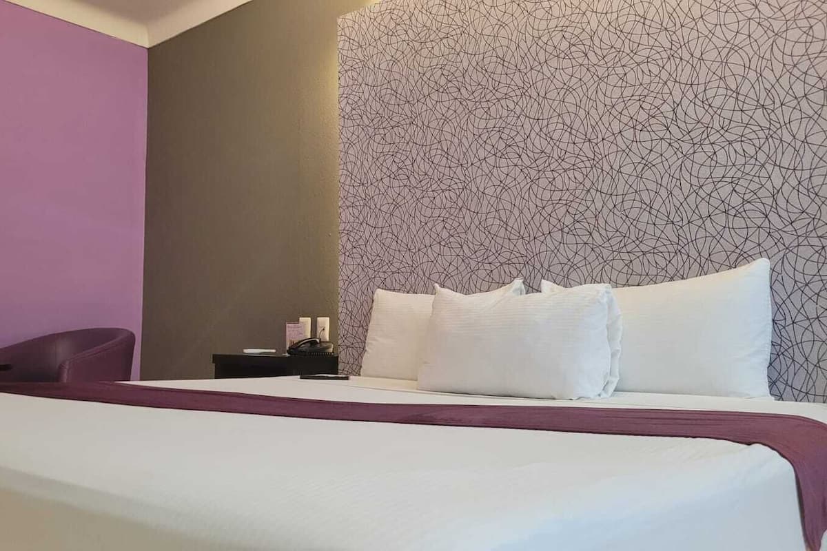 A hotel room with a large bed, a desk with a chair, and a purple wall.