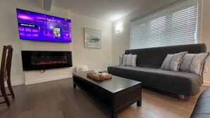 A living room with a flat-screen TV mounted on the wall, a fireplace below it, a dark-colored sofa with striped pillows, a wooden coffee table, and a ceiling fan. - Cabin in South Beach - Steps from the beach (Gimli)