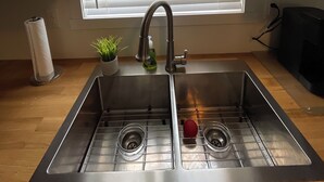 A kitchen with a double sink, stainless steel appliances, a potted plant, and a window with blinds. - Cabin in South Beach - Steps from the beach (Gimli)
