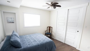 A bedroom with a bed, a chair, a window, and a door. - Cabin in South Beach - Steps from the beach (Gimli)