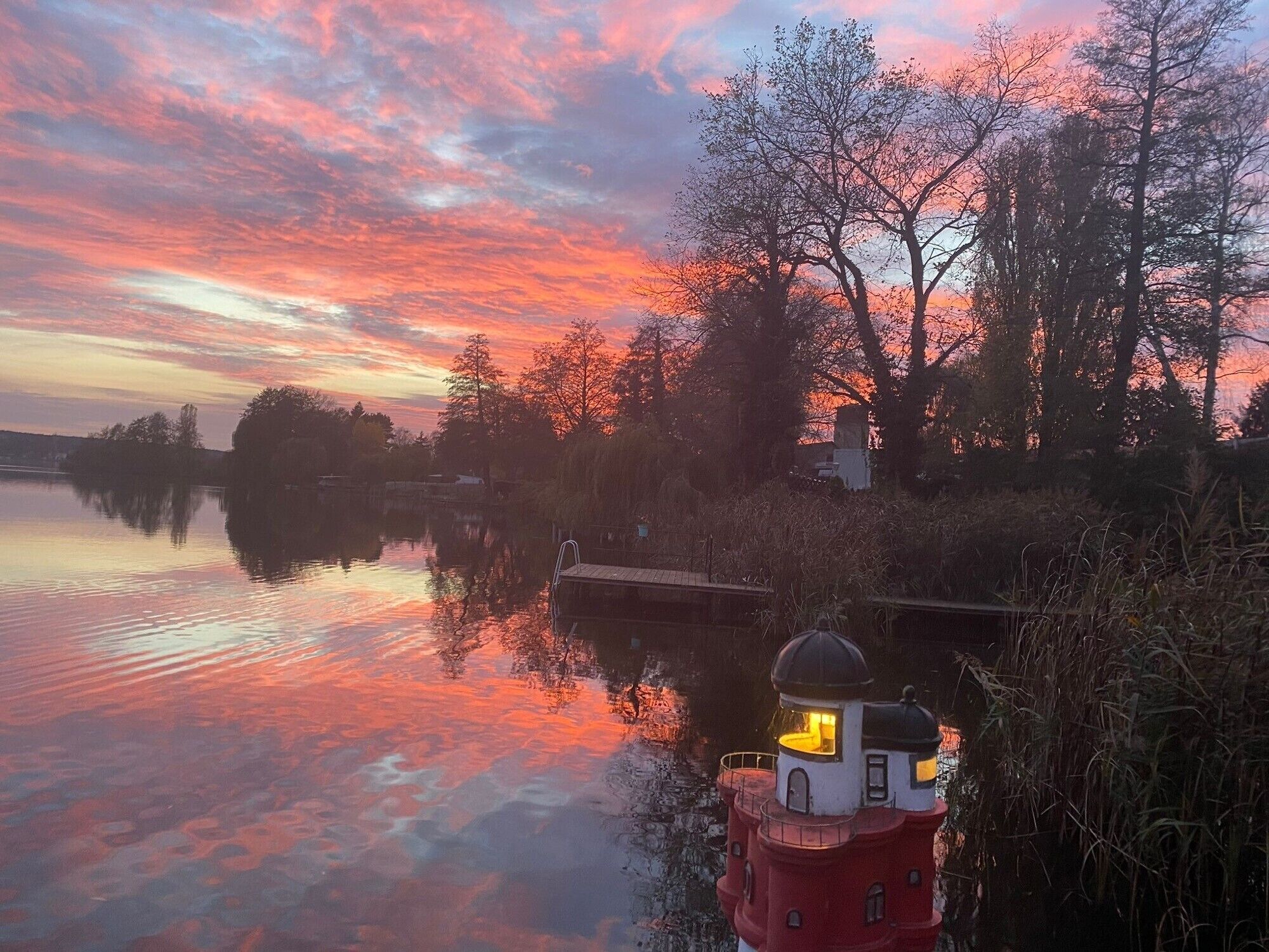 Un faro rosso con una cupola, affacciato su un'acqua calma che riflette il cielo.
