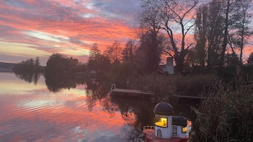 Un faro rosso con una cupola, affacciato su un'acqua calma che riflette il cielo.