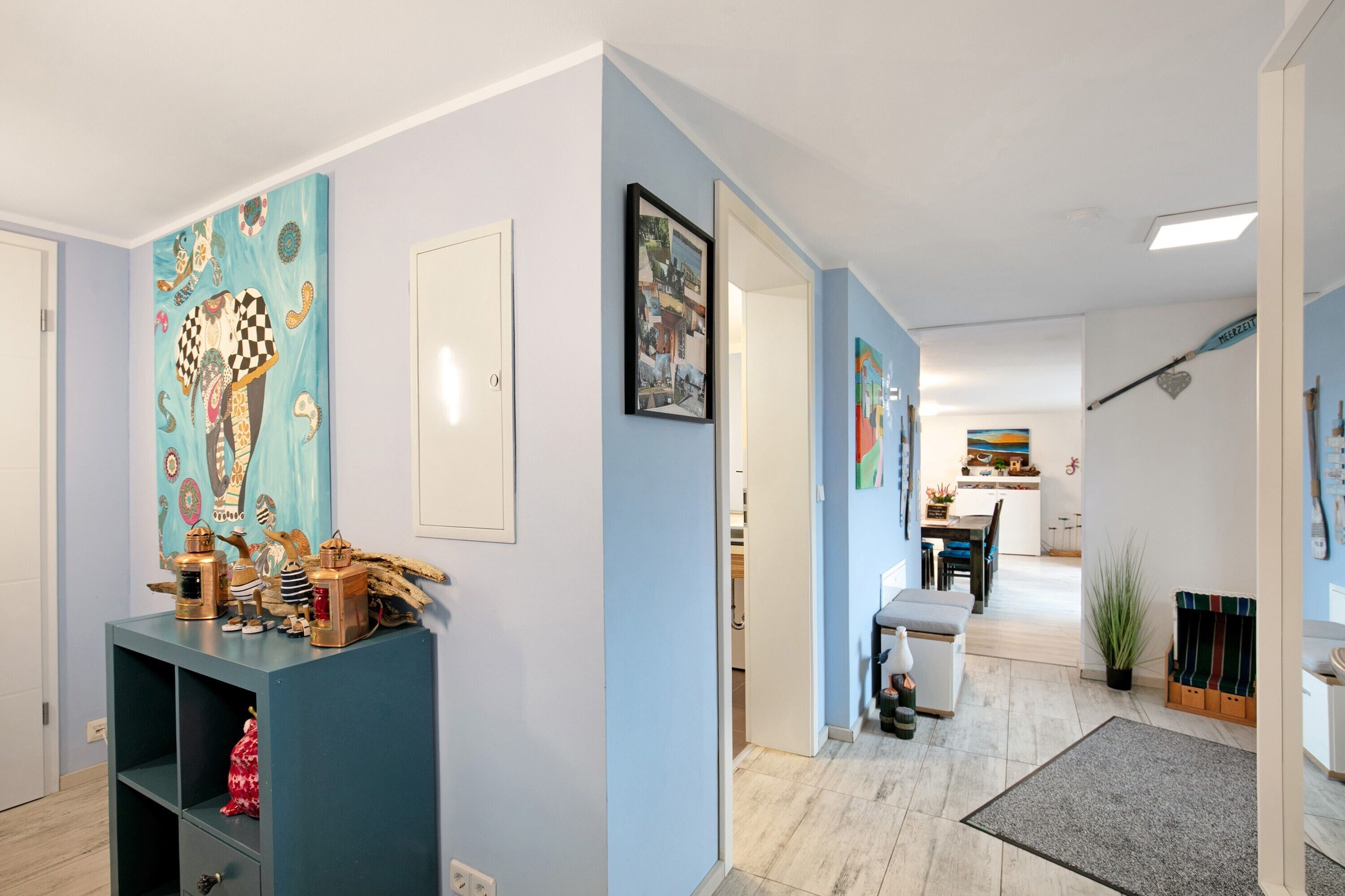 Ein Flur mit blauer Wand, einem Holzkabinett mit Dekoration und einem gerahmten Bild.