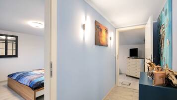 A bedroom with a bed, a painting, a dresser, and a television in the adjacent room.
