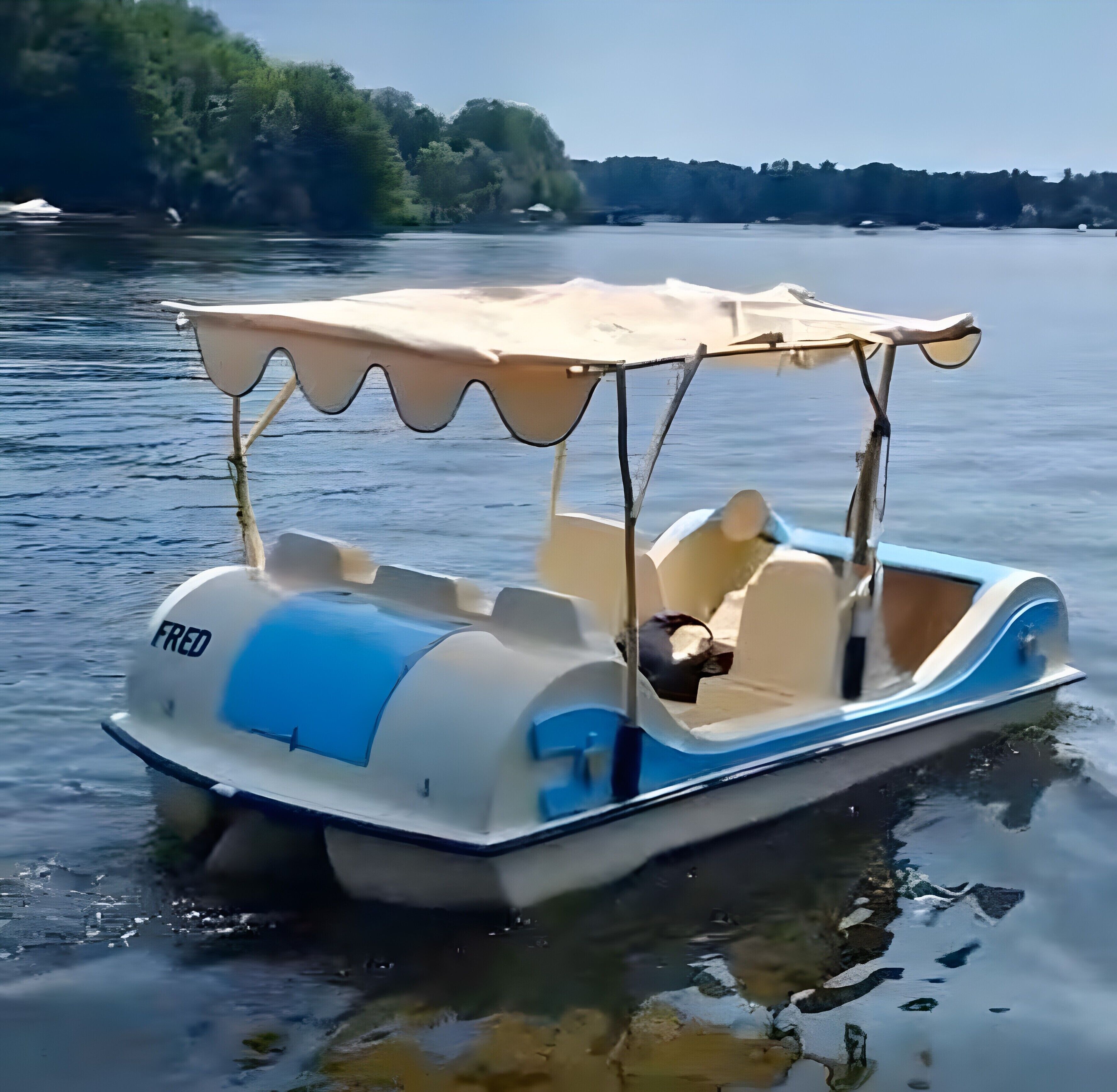 Un petit bateau à moteur doté d’une cabine, d’une bande bleue et du nom « FRED » à l’arrière.